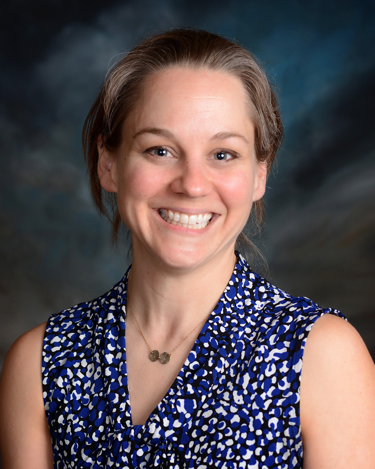 White woman with blond hair, pulled back, and floral shirt; smiling