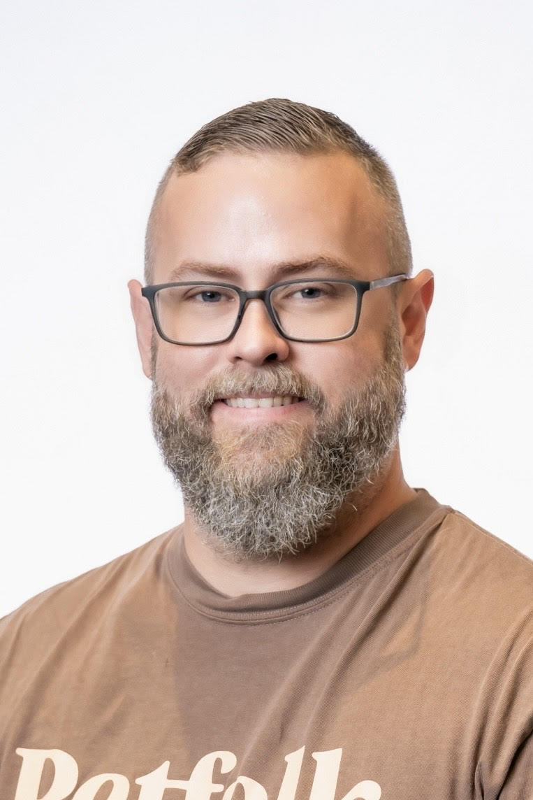 White male with glasses, beard, and tan shirt; smiling