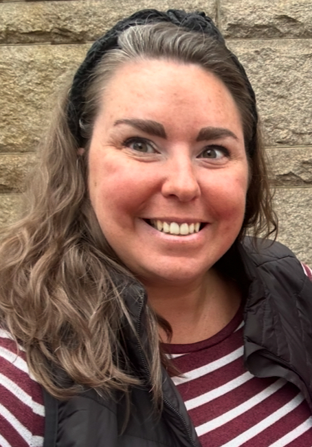 White woman with brown hair pulled back in a headband, striped maroon shirt; smiling